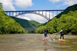 Paddle-boarders navigate toward New River Gorge Bridge