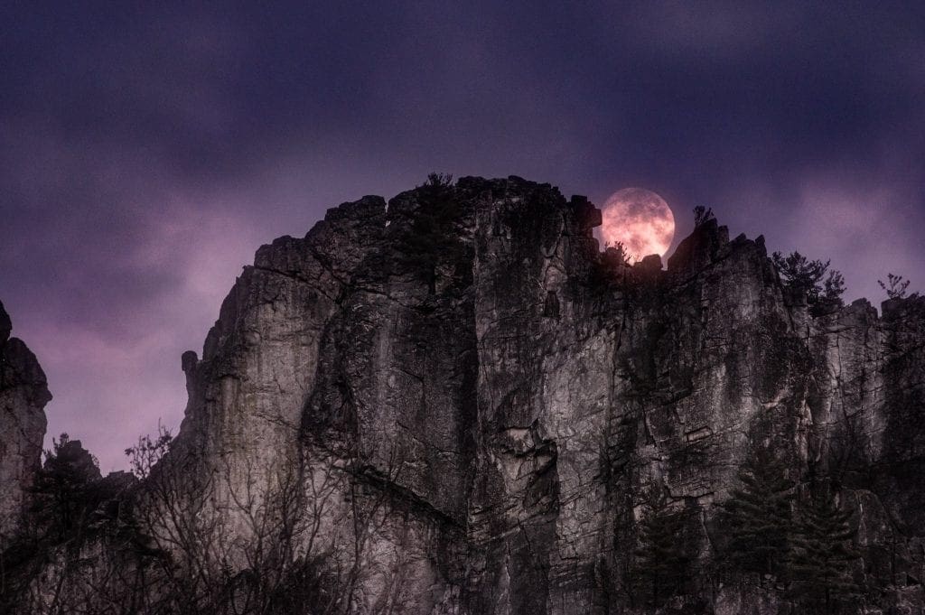A full moon peeks over the towering blade of Seneca Rocks.