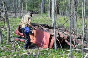 Justyn Marchese examines the remains of a vehicle abandoned in a remote farmstead area on the Polls Plateau Trail.