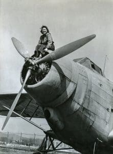 An unidentified employ sits on the nose cowl of an aircraft at the ordnance center.